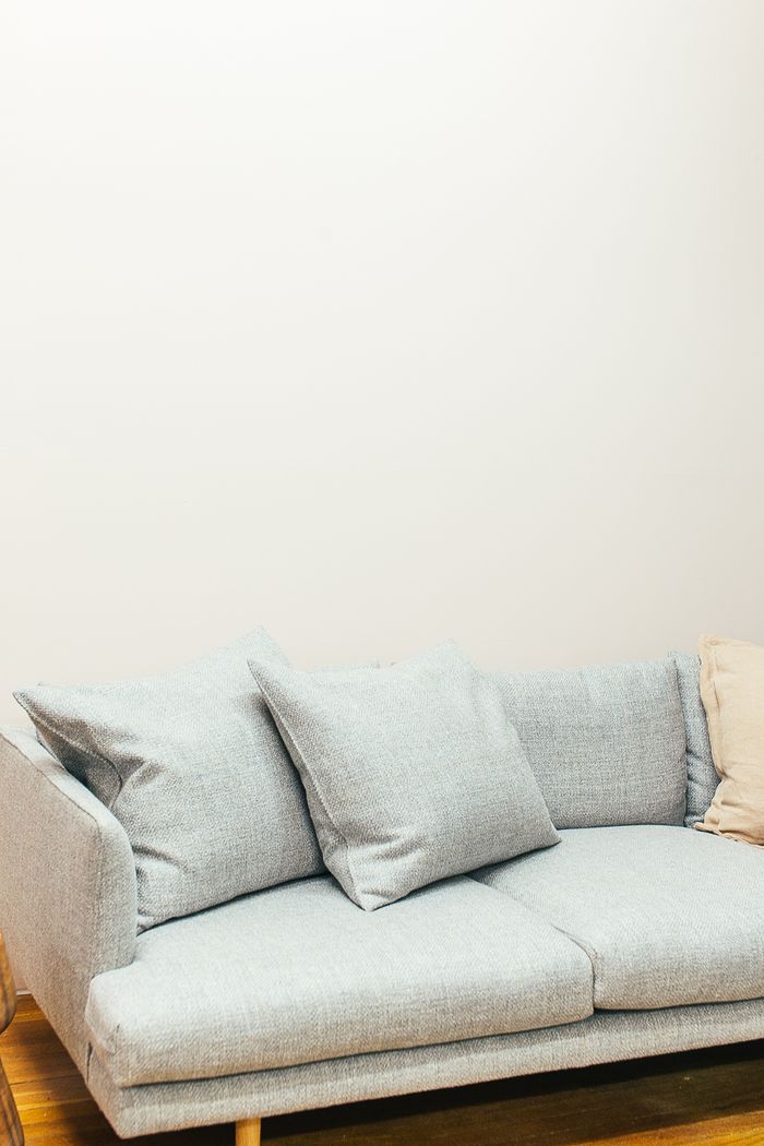 Soft couch with pillows placed in light living room on wooden floor near white wall